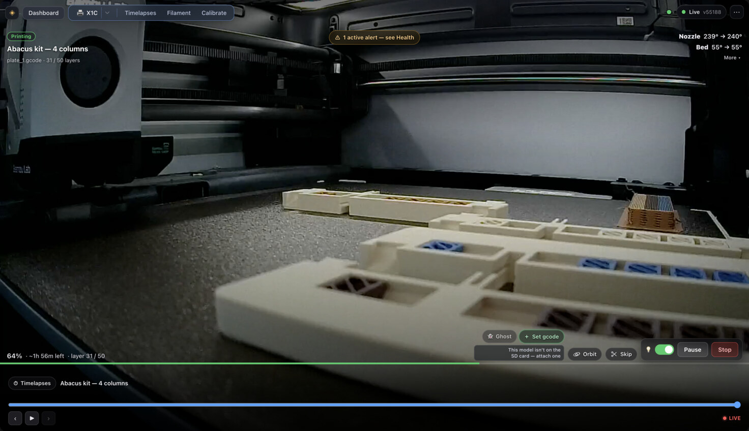 Self-hosted cockpit for an X1C mid-print: the chamber camera fills the frame, showing finished abacus rails with blue and brown beads sitting on the bed. A &ldquo;Printing&rdquo; badge sits over the job name &ldquo;Abacus kit — 4 columns&rdquo;, with the nozzle at 239° climbing to 240°, and 64% complete at layer 31 of 50.